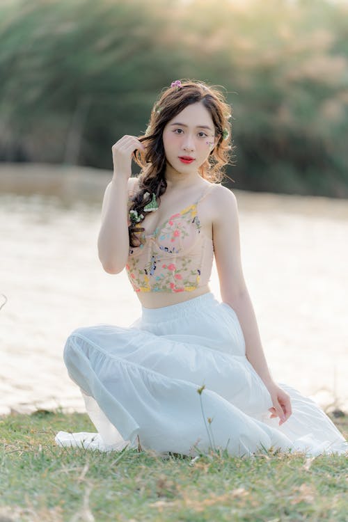A beautiful young woman in a white top and skirt sitting on the grass