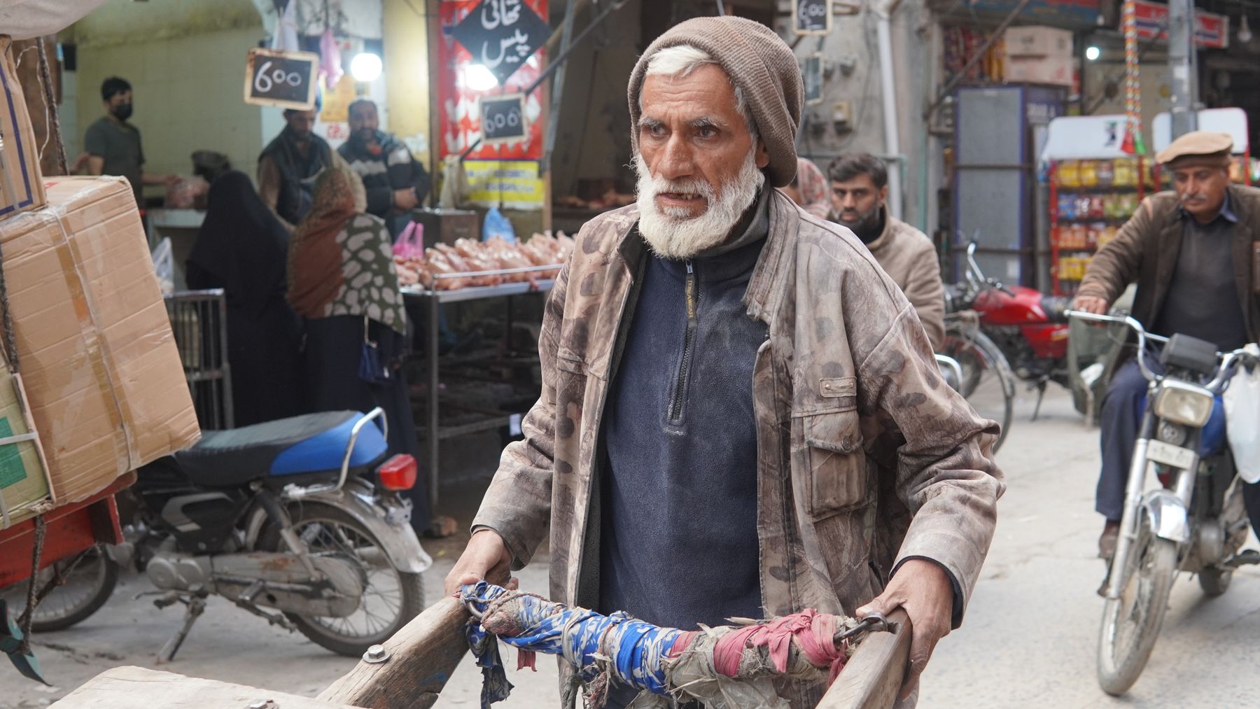An elderly man pulling a cart through a busy marketplace in Rawalpindi, Pakistan.