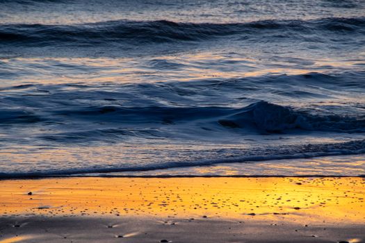 A serene sunset at an Orleans beach with golden reflections on the waves.