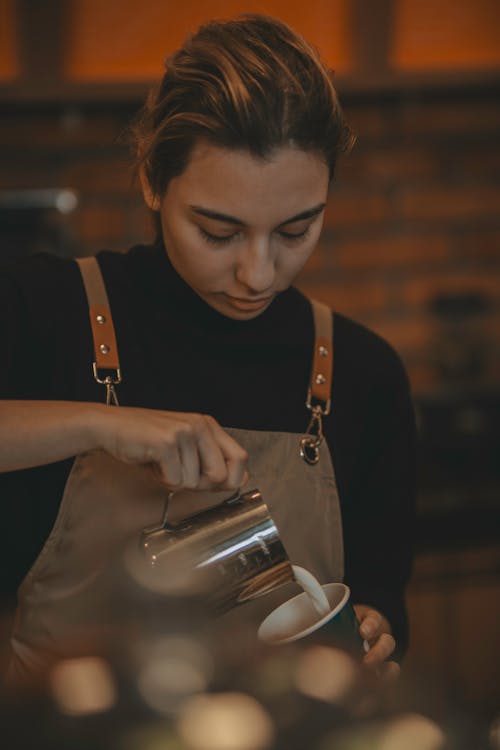 A woman in an apron pouring coffee into a cup