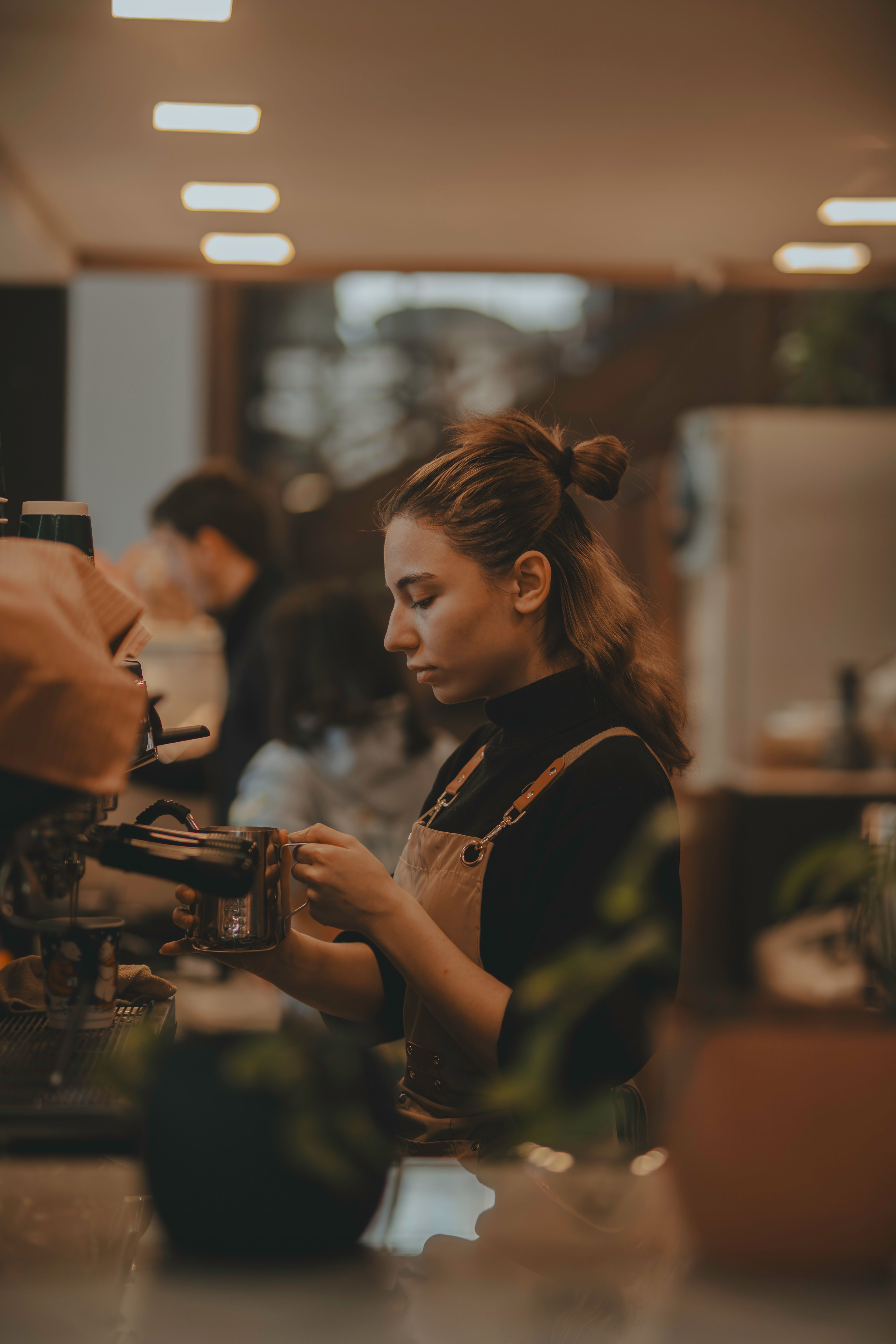A barista focused on a pour at the counter in warm light