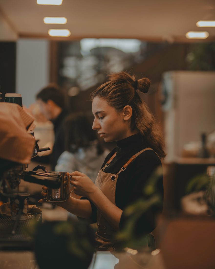 A barista focused on a pour at the counter in warm light