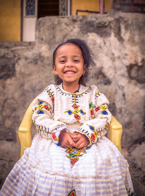 A smiling little girl in a traditional dress sitting on a chair
