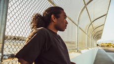 一名男子若有所思地站在城市户外环境的铁丝网围栏旁