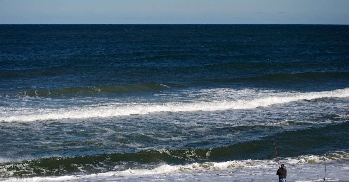 A lone fisherman casts a line on Nags Head beach, North Carolina, with waves crashing on the shore.