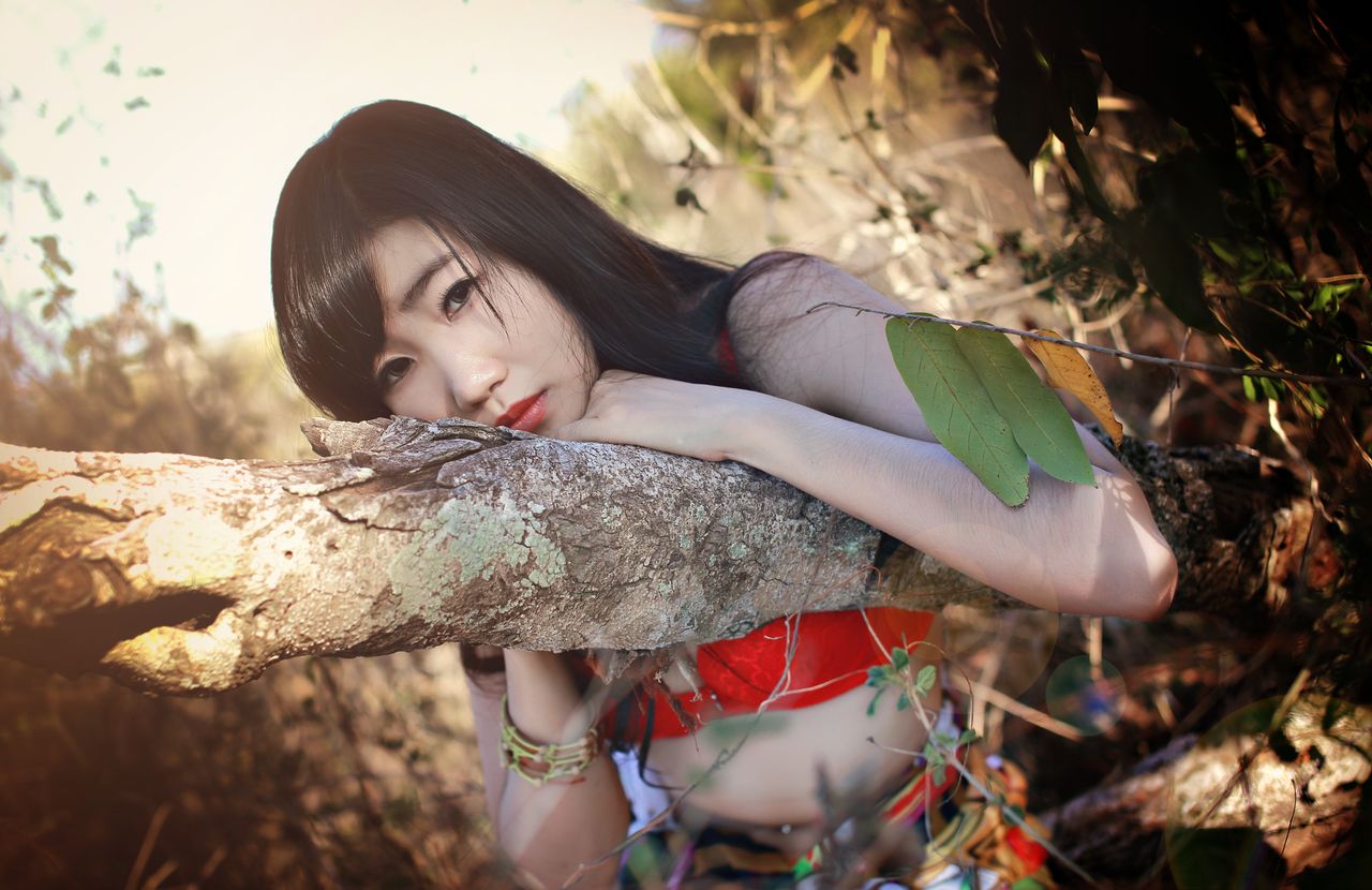 elegant young woman leaning on a tree trunk surrounded by vibrant foli