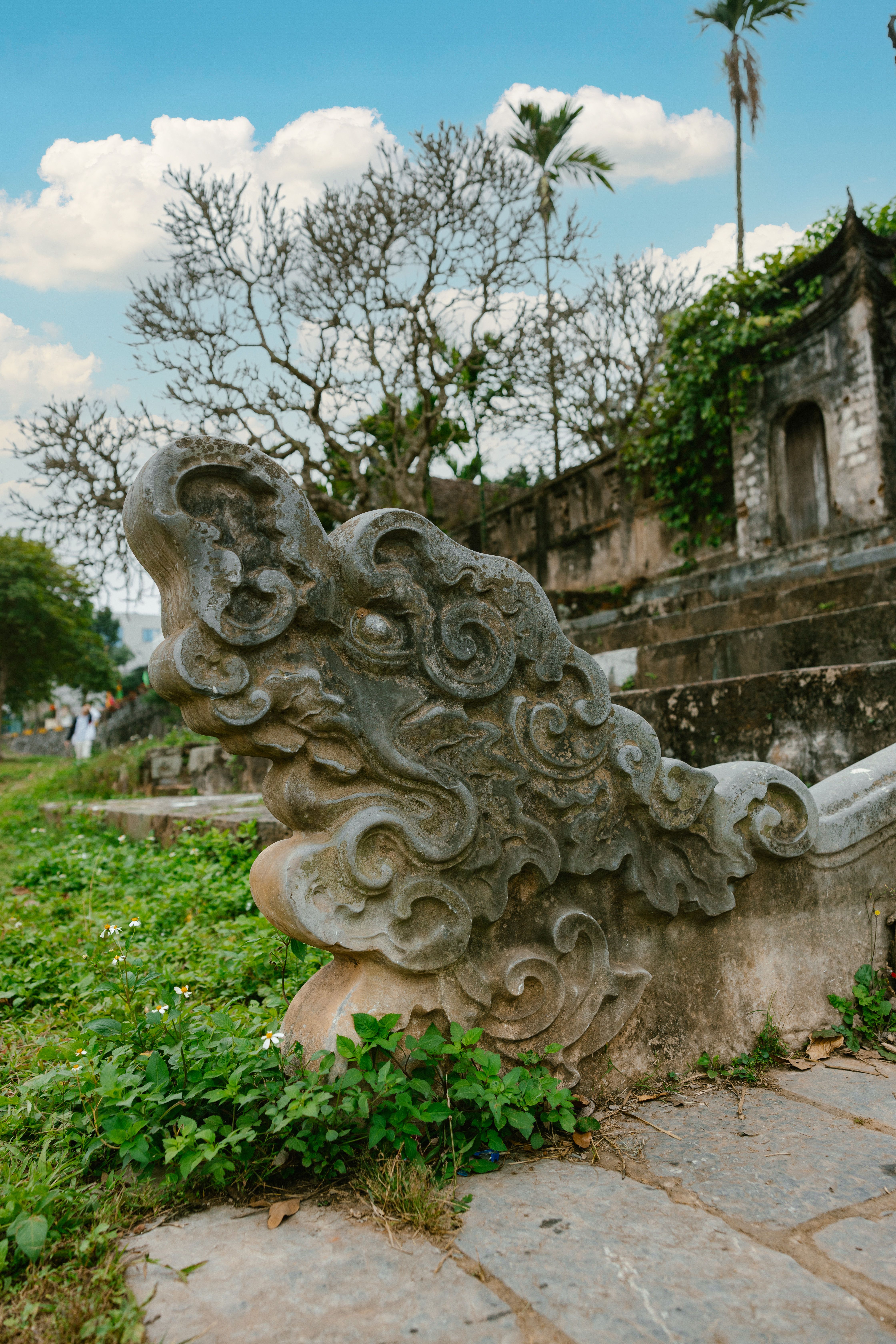 Ornate stone sculpture in a lush green temple environment under a clear blue sky.