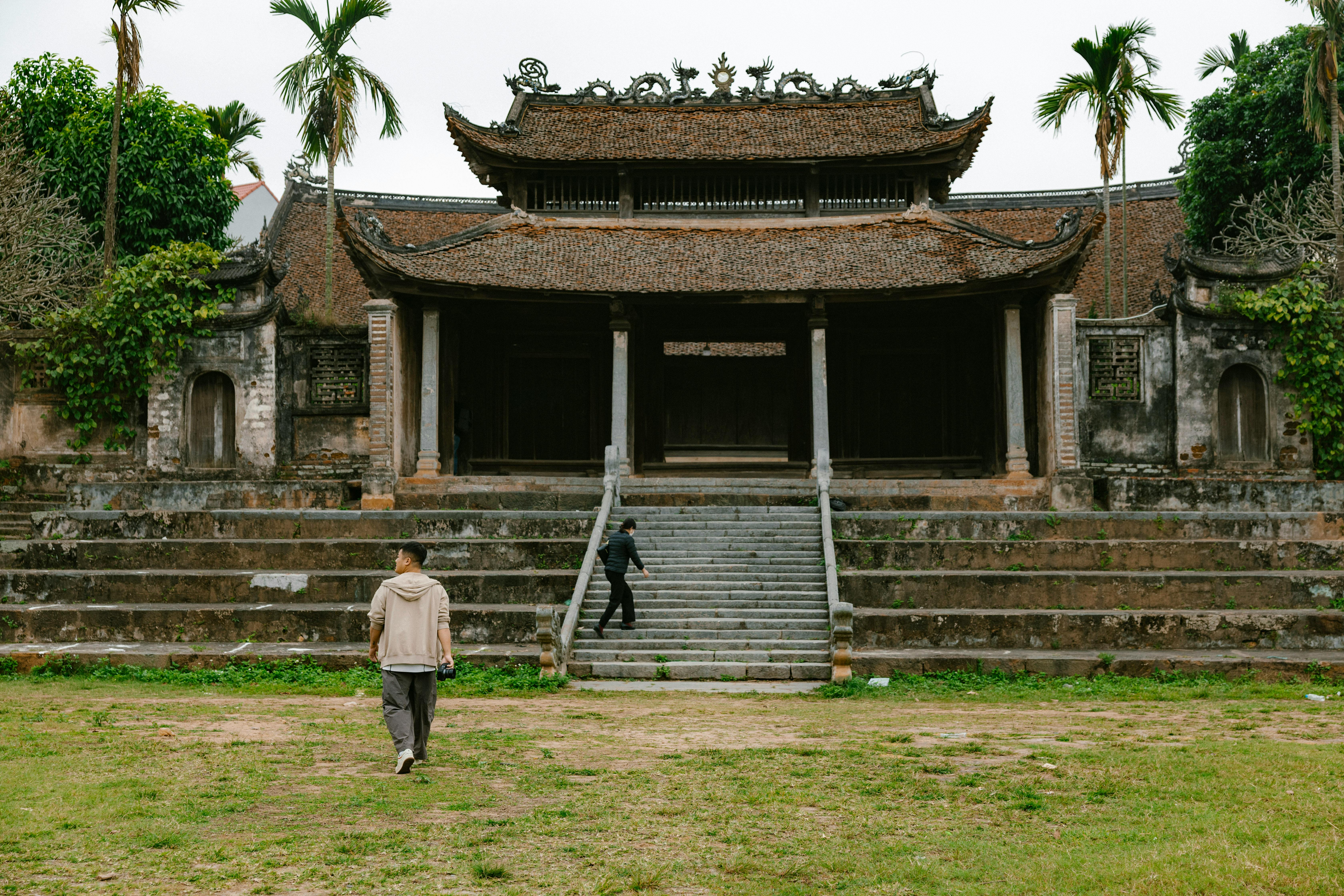 Historic Vietnamese temple facade with palm trees and visitors during daytime.