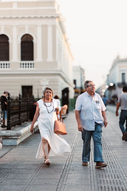 Free A cheerful elderly couple walks through a sunny city street, capturing urban lifestyle. Stock Photo
