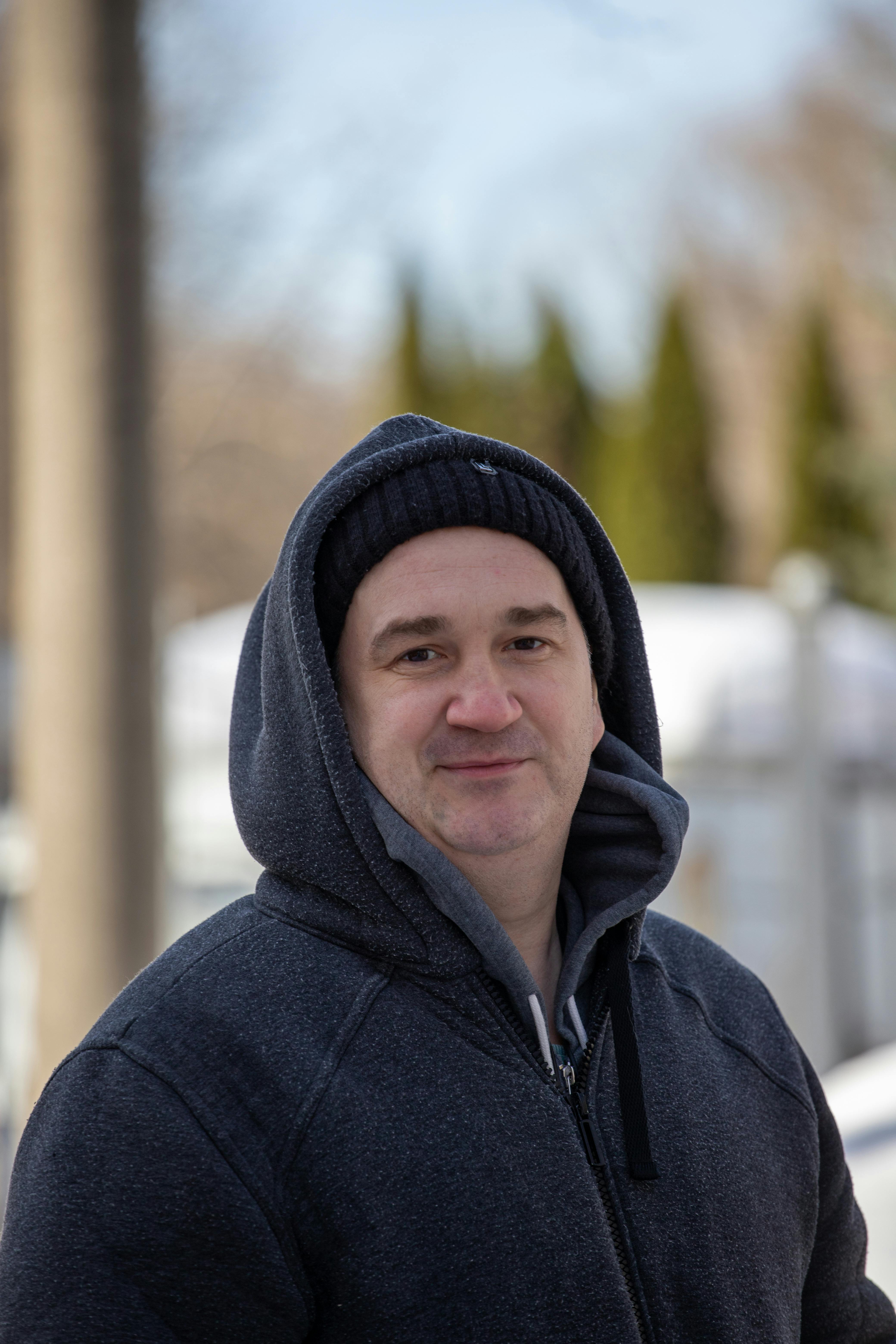 Smiling man wearing a hoodie and beanie outdoors in winter. Casual and warm appearance.