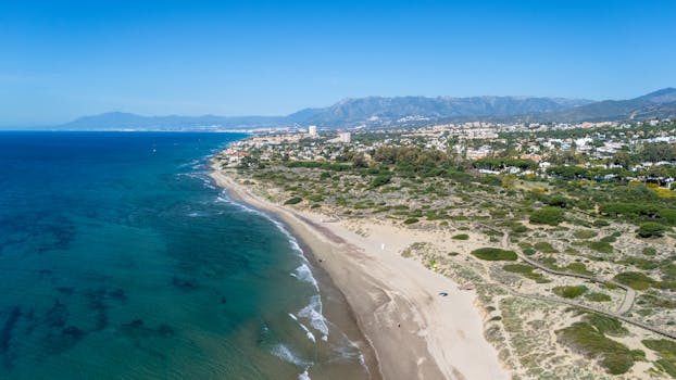 Drone shot of serene Bolonia beach, Spain, featuring clear blue waters and coastal landscape.