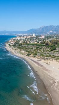 Stunning aerial view of a beach coastline adjacent to a vibrant city with mountain backdrop.