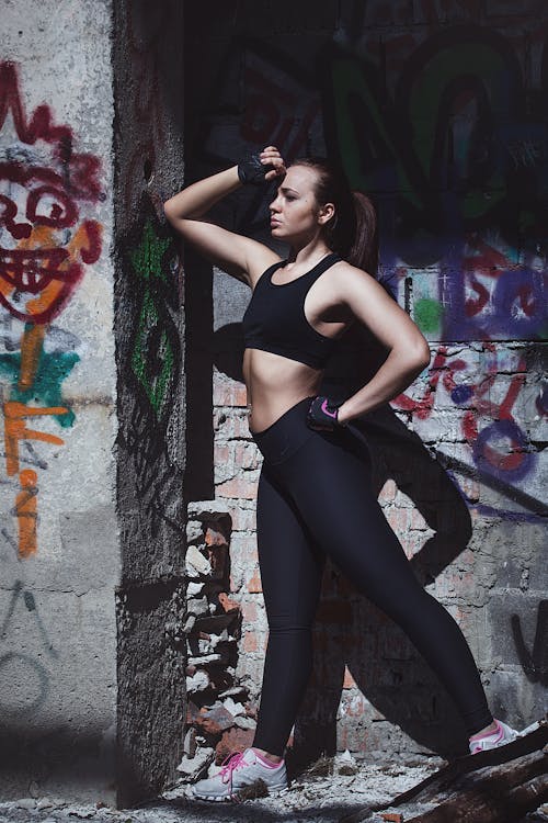 Free Woman in Sports Bra and Leggings Standing by the Wall Stock Photo