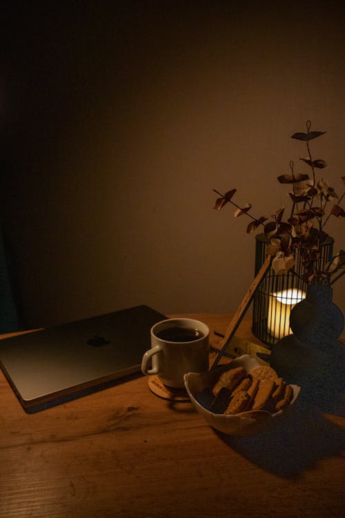 A laptop on a table with a candle and a cup of coffee