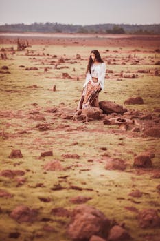 A woman elegantly poses in a vast rocky field, showcasing a serene outdoor scene.
