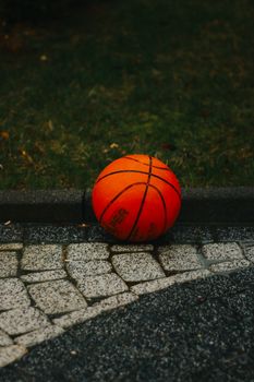 Close-up of a vibrant orange basketball resting on stone pavement with a grassy background.