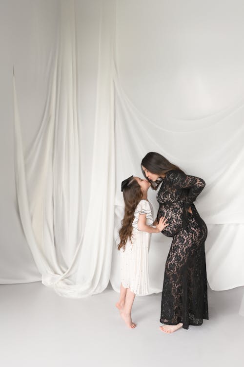 A woman and her daughter pose for a photo in front of a white backdrop