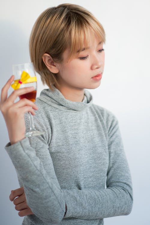 Woman Holding Wine Glass Standing Beside White Wall