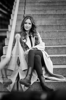 A fashionable woman in a coat and boots posing elegantly on city steps, reflecting urban style.