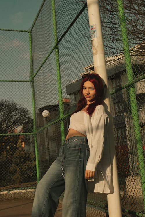 A woman in jeans leaning against a fence