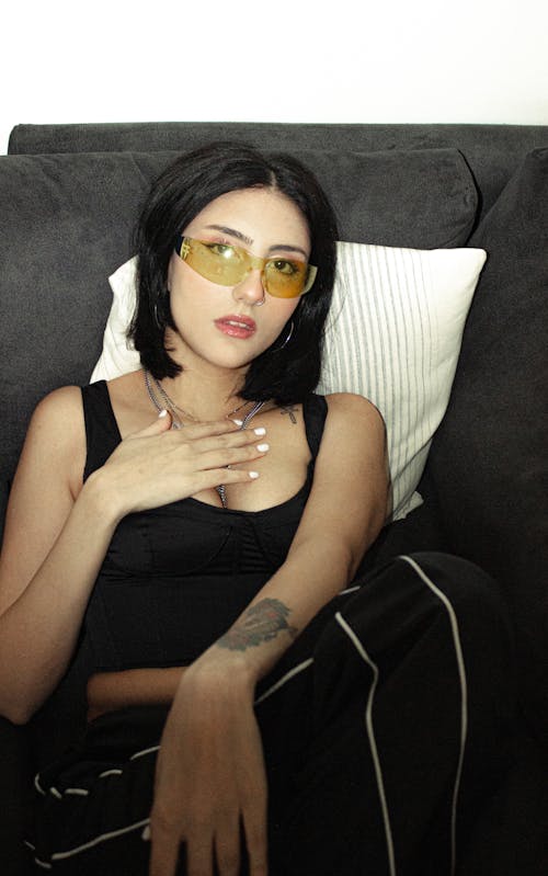 A woman in black and yellow sunglasses sitting on a couch