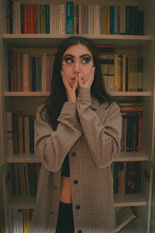 A woman is covering her face in front of a book shelf