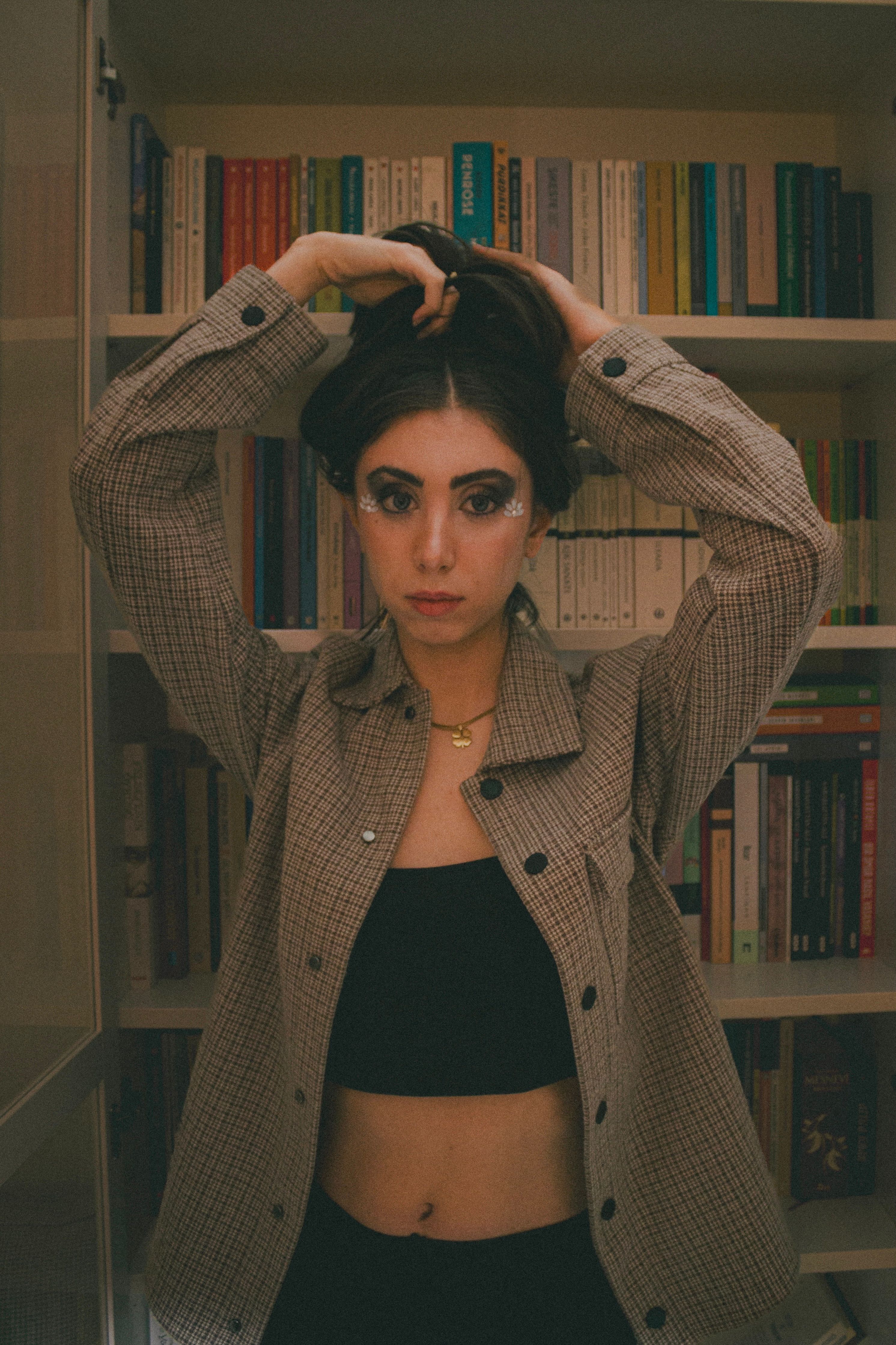 Young woman fixing hair while standing in trendy outfit, Ankara library.