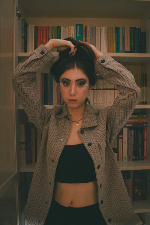 A woman in a jacket and top posing in front of bookshelves