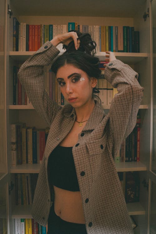 A woman in a jacket and top standing in front of bookshelves