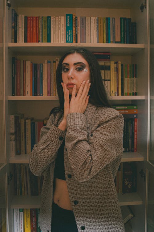 A woman in front of a book shelf with her hands on her face