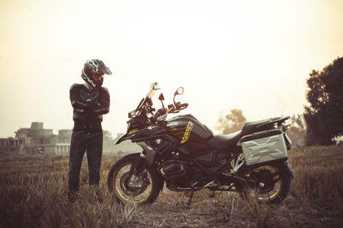 Free A motorcyclist standing near an adventure bike in a grassy field during daytime. Stock Photo