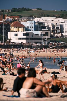 Sunny day at Bondi Beach with bustling crowds enjoying the seaside and view of nearby buildings.