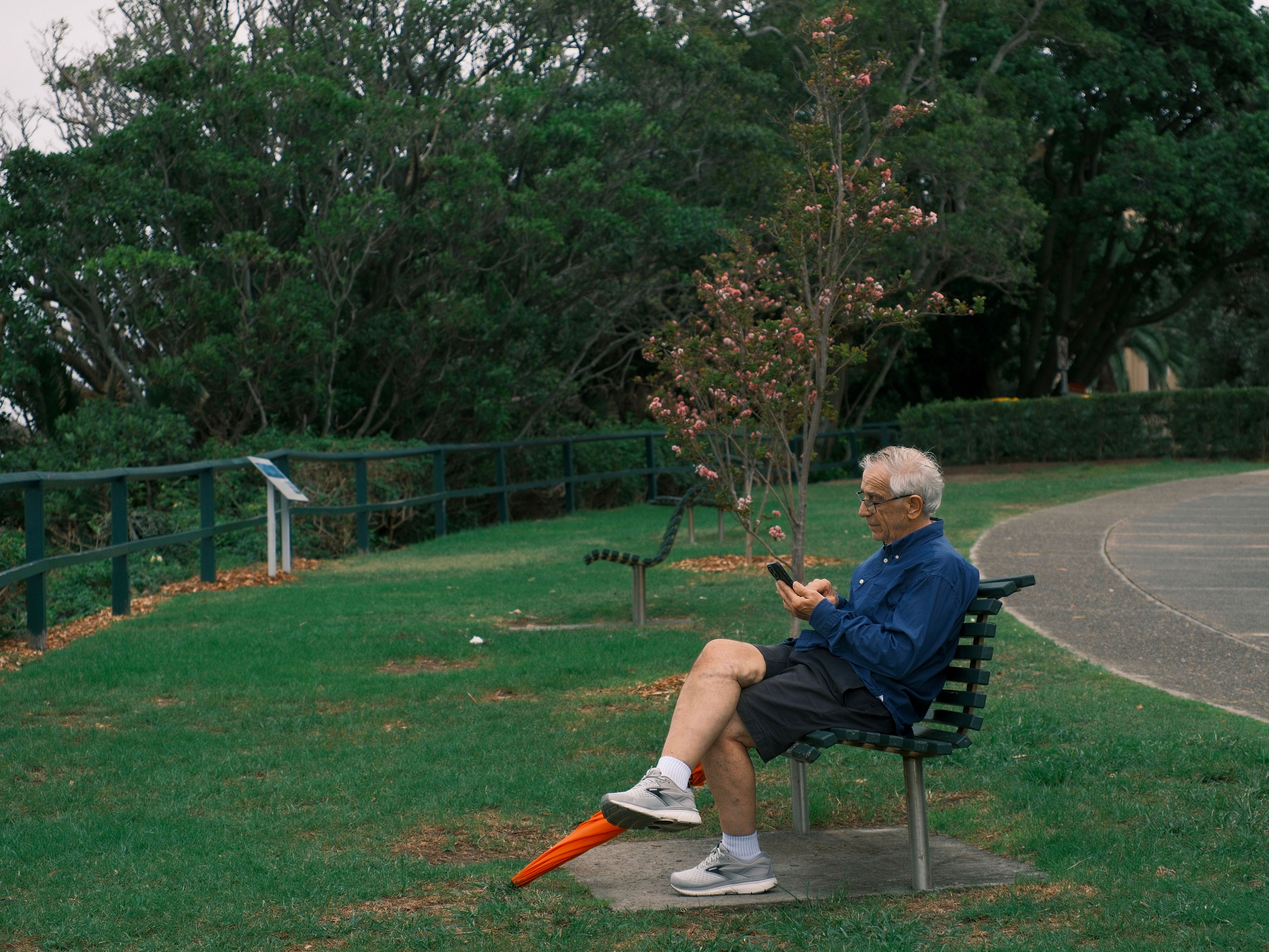 Elderly man sitting on bench in park, engaged with smartphone technology.