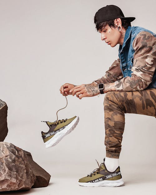 A man in camouflage pants and sneakers is holding a pair of sneakers