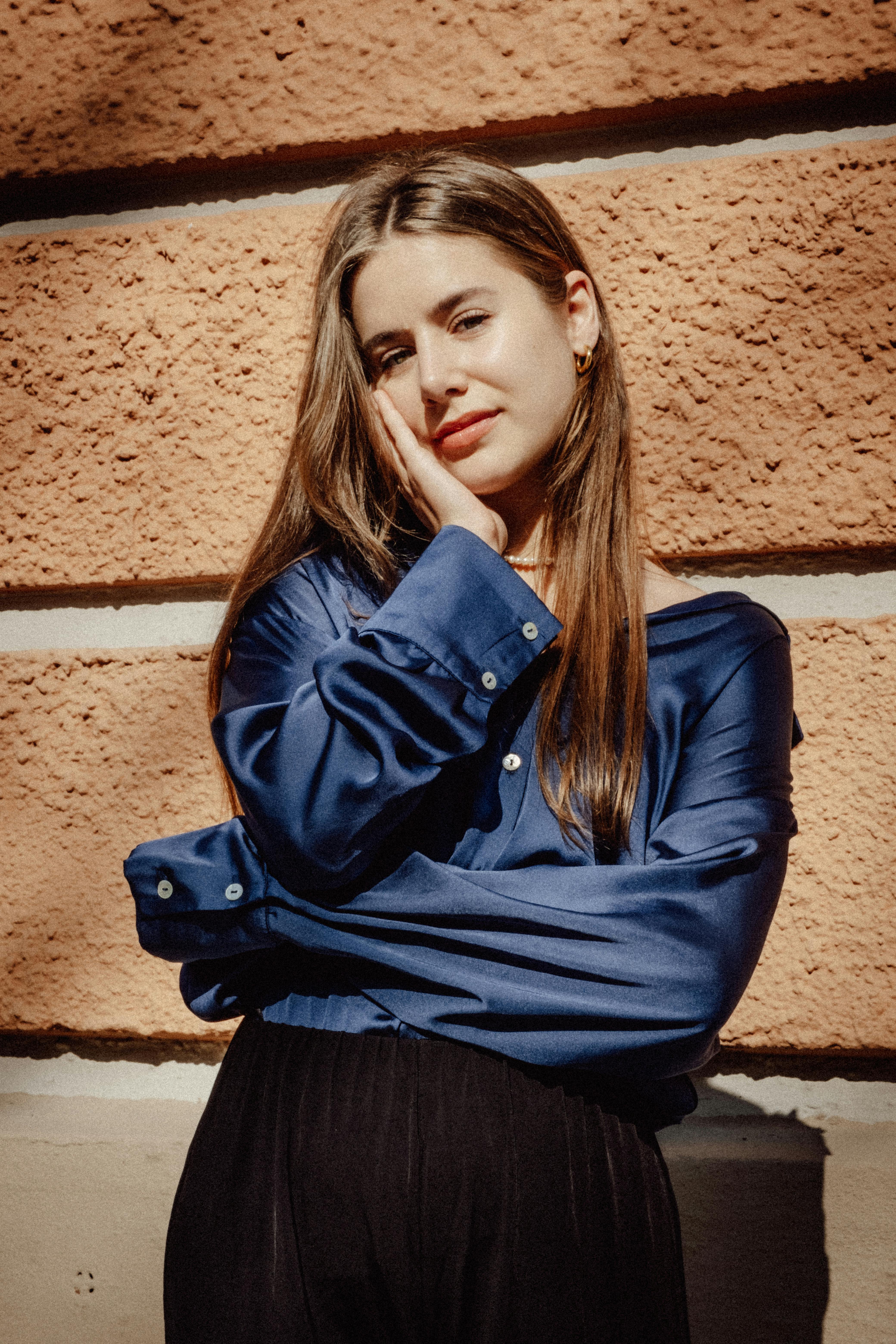 Portrait of a stylish brunette woman posing confidently against a textured urban wall.