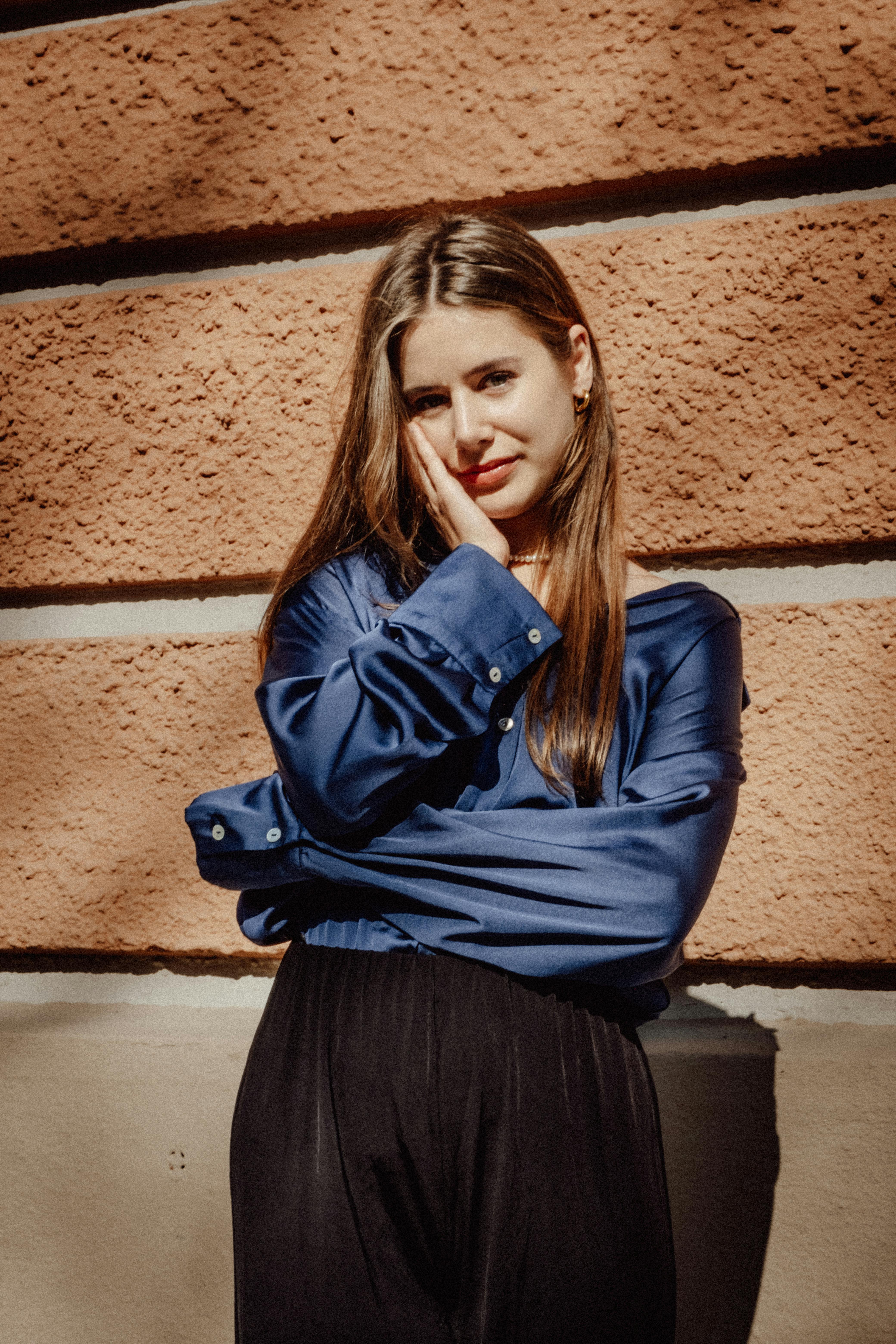 Stylish woman in blue blouse posing outdoors against a warm-toned brick wall.