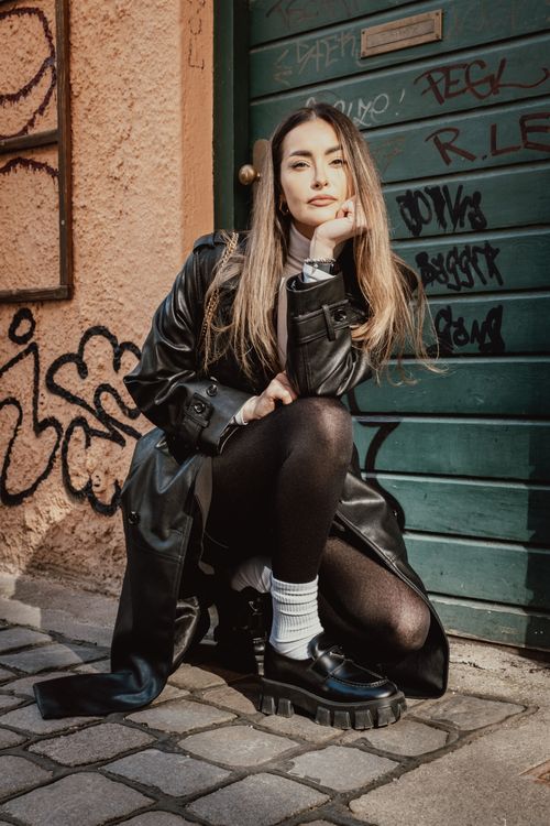 Free A fashionable woman poses stylishly in urban setting with graffiti backdrop. Stock Photo