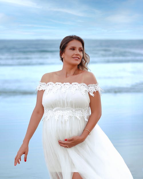 A pregnant woman in a white dress on the beach