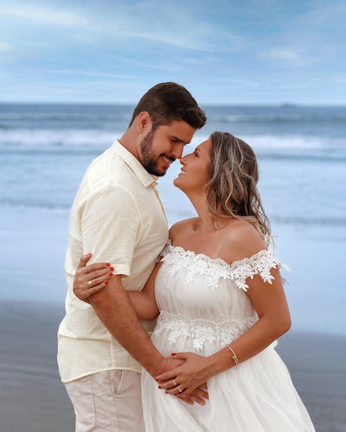 A pregnant woman and her husband are standing on the beach