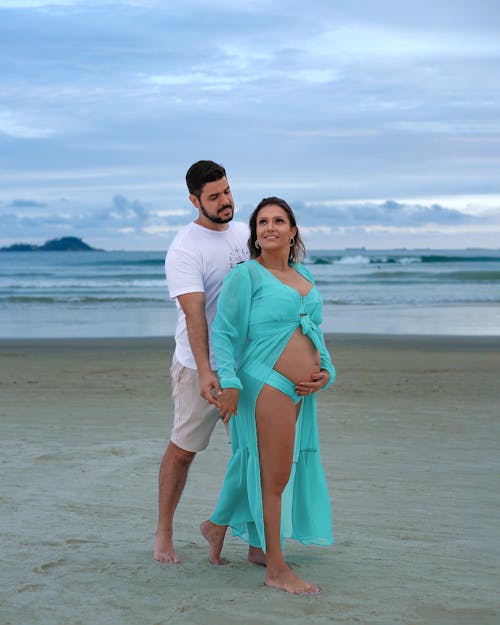 A pregnant woman and her husband standing on the beach