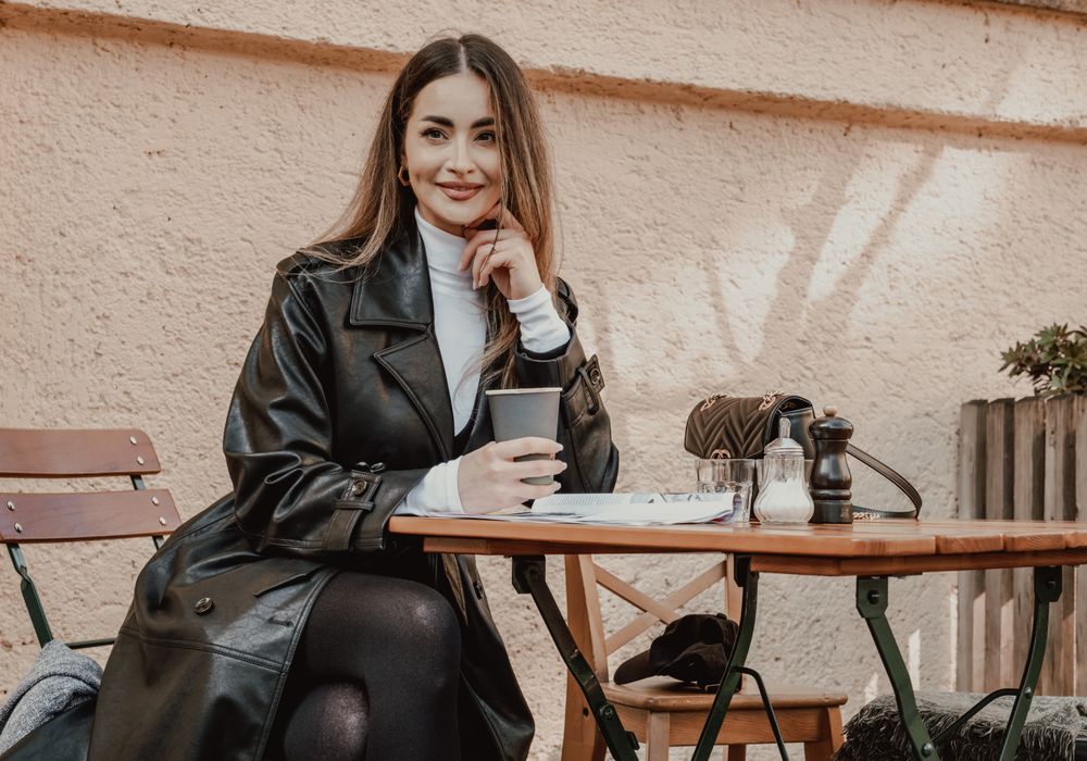 Woman in a leather coat having coffee at a cafe table