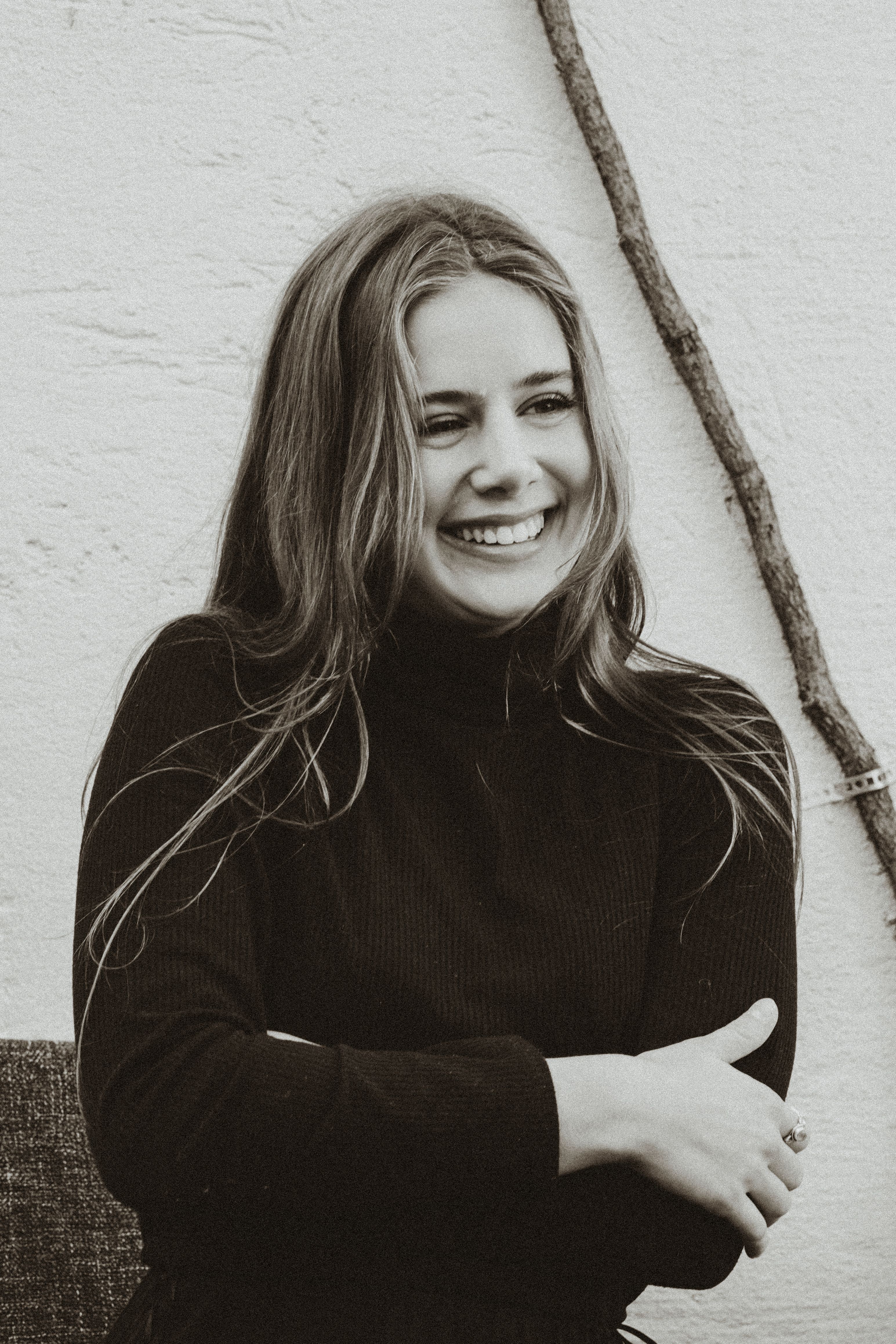 Monochrome portrait of a smiling woman with long hair and arms crossed.