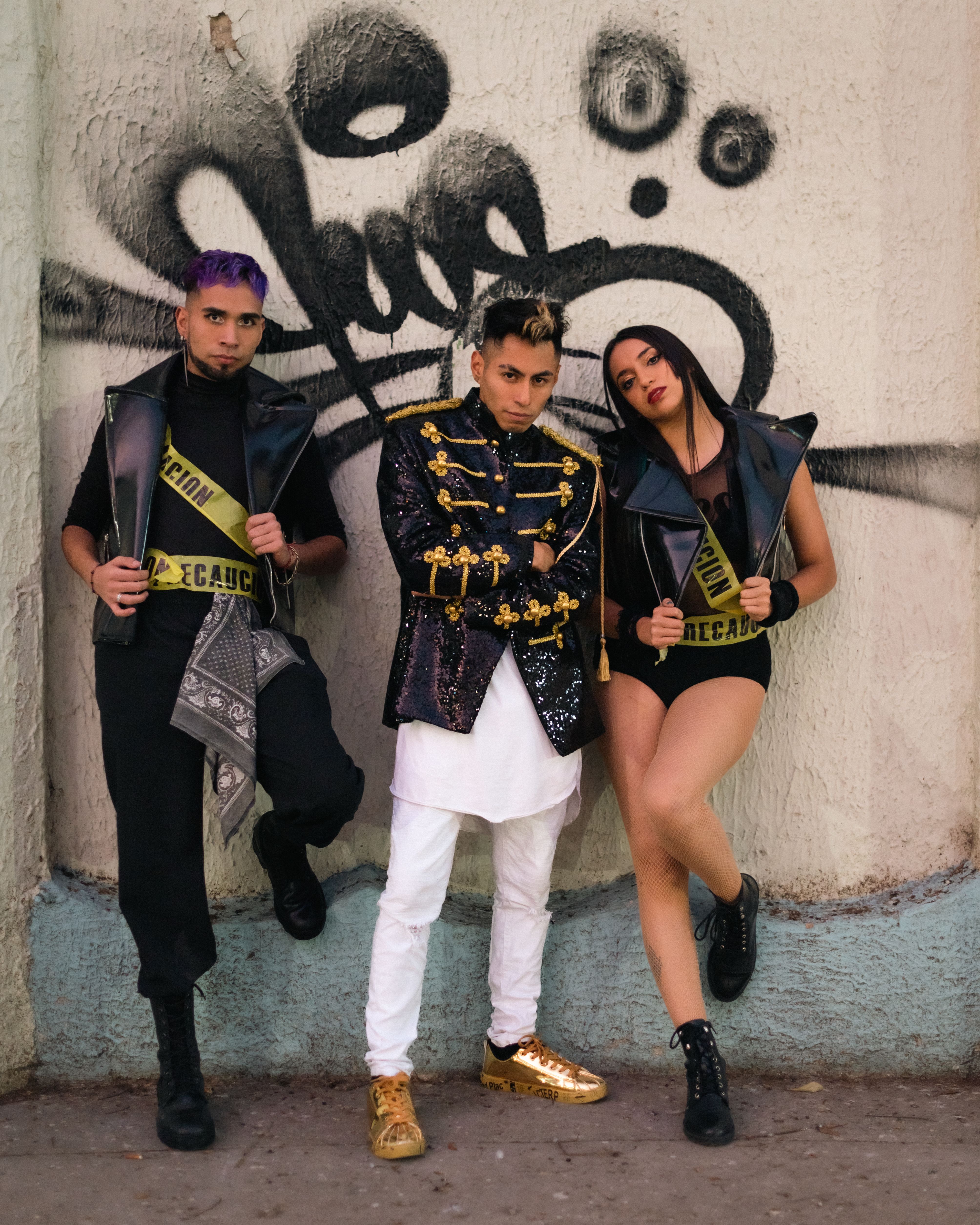 Three people posing in stylish outfits against a graffiti wall in Ciudad de México.