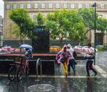 People walking on a wet city sidewalk during a rainstorm, carrying umbrellas and wearing ponchos.