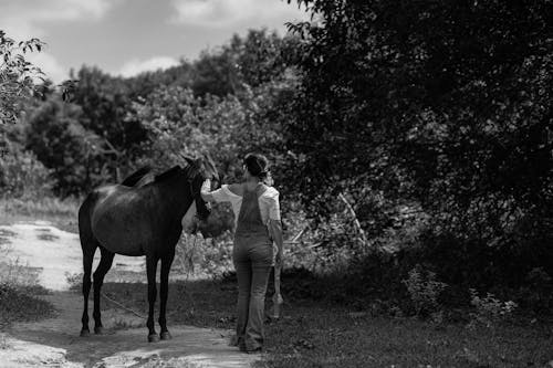 A woman is standing next to a horse on a dirt road