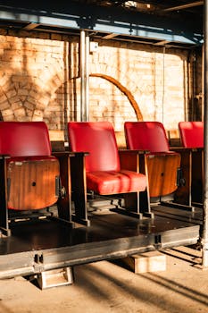 A row of red vintage theater seats in an industrial setting with warm sunlight casting shadows.
