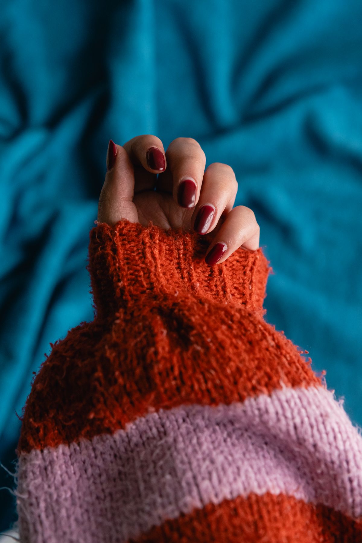 A hand with red nails partially hidden in a red and pink striped sweater against a blue background.