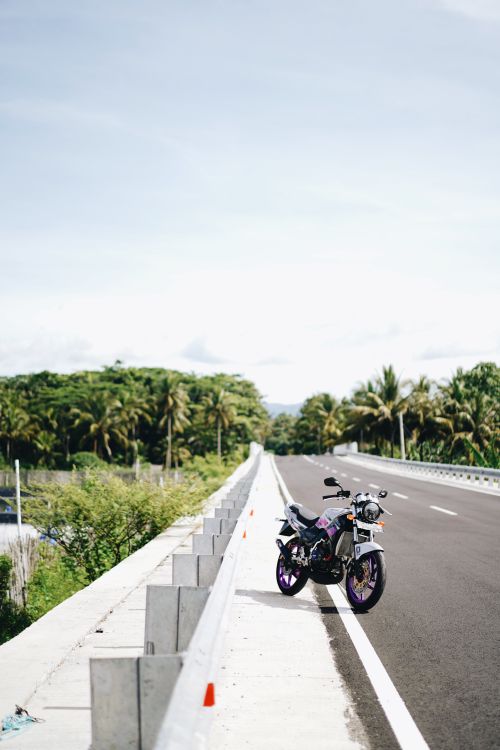 Free A motorcycle parked on a roadside with a view of lush green forest under a bright sky. Stock Photo