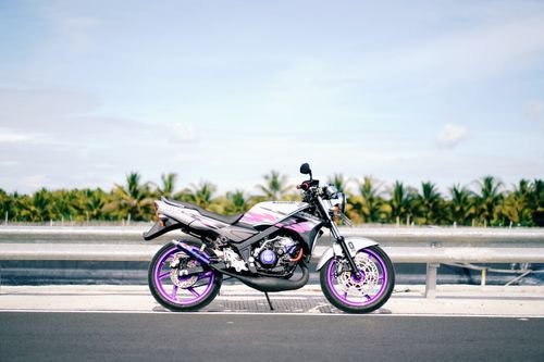 Free A vibrant Kawasaki motorcycle parked on a sunny road with palm trees in the background. Stock Photo