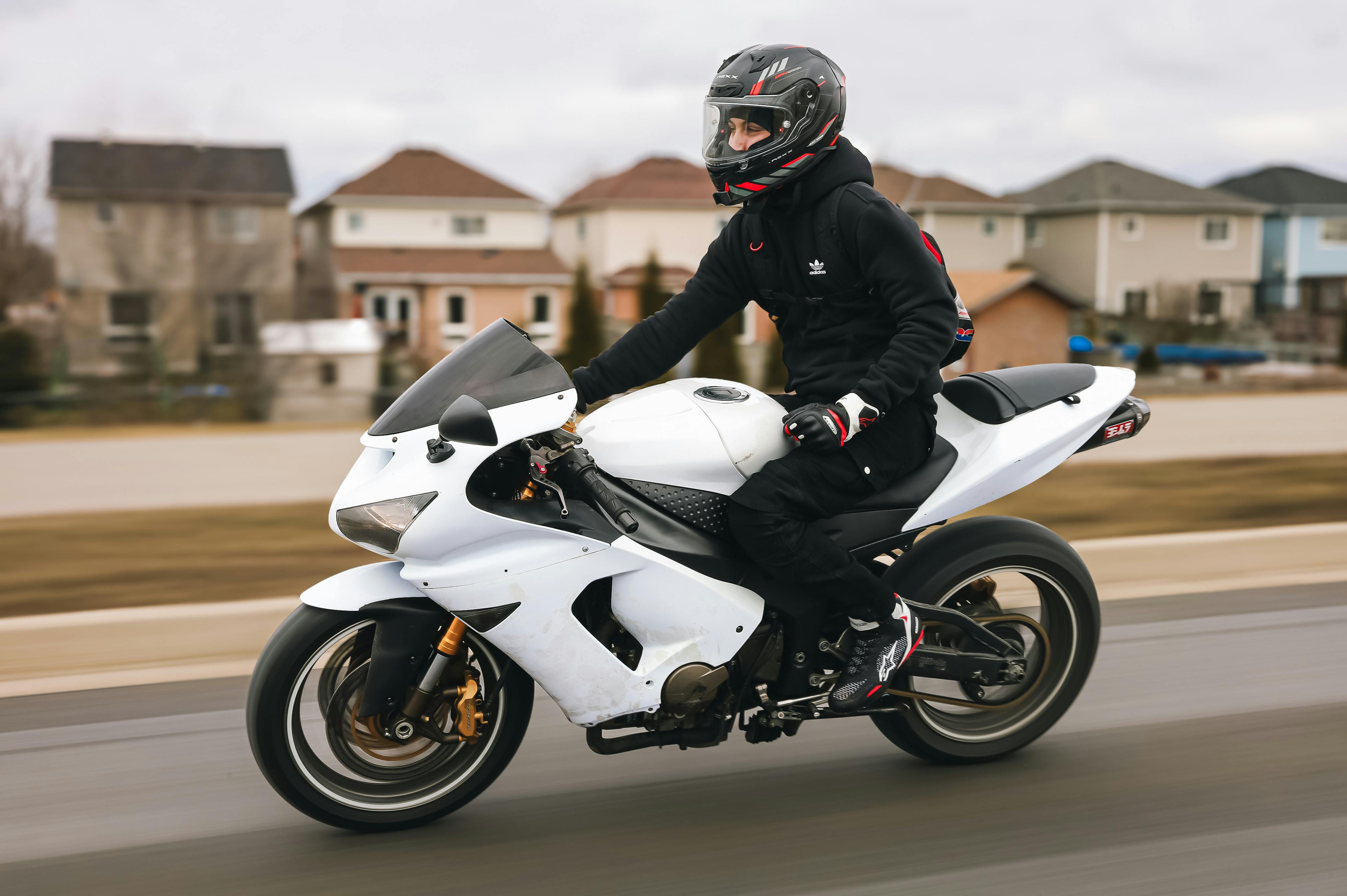 Motorcyclist wearing black gear rides a white sportbike on an urban road, showcasing speed and motion.